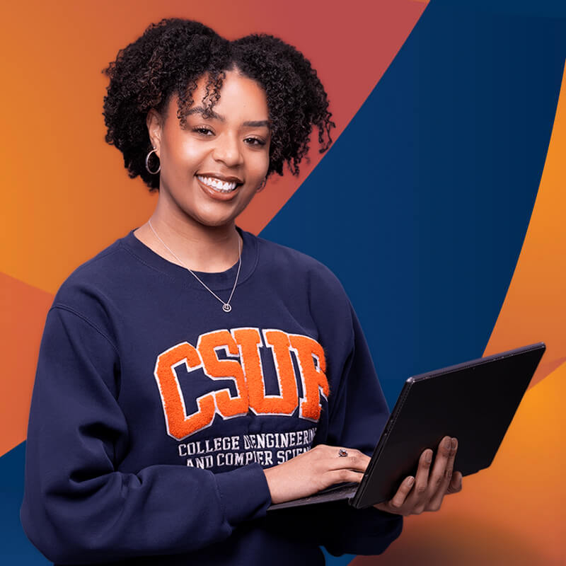 Woman wearing a CSUF sweatshirt holding a laptop and smiling, standing against an orange and blue background.
